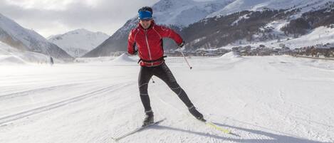 A person cross-country skiing on a snowy path with mountains in the background.