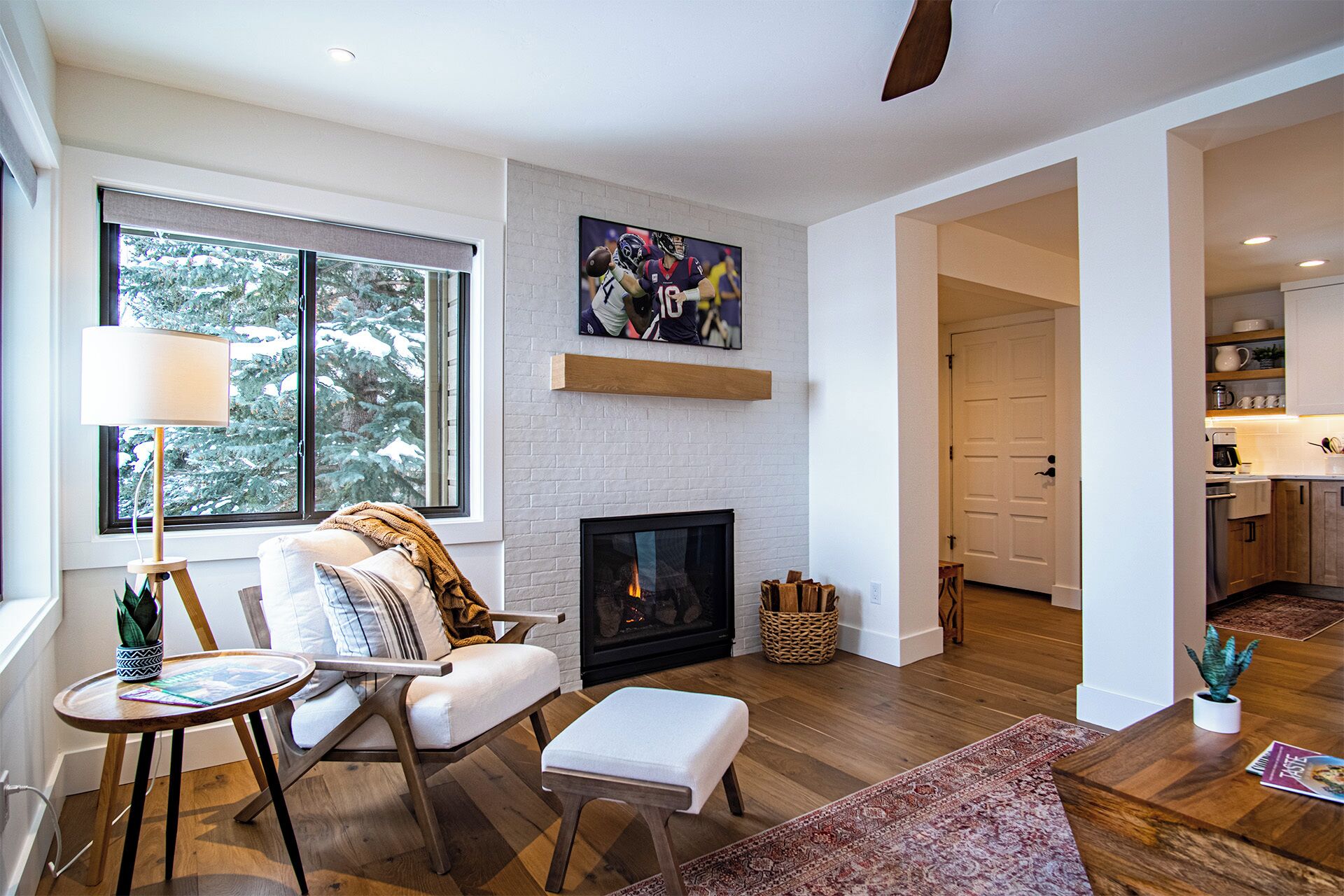 A modern living room with a fireplace, a television mounted above it, and a cozy seating area with a chair and ottoman.