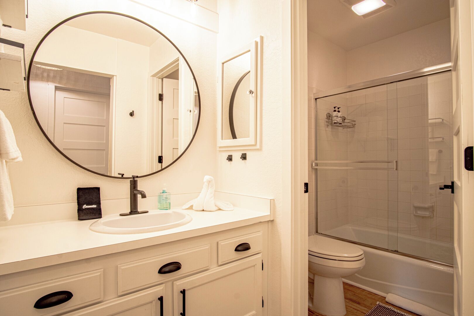 A bathroom with a round mirror, a sink, a toilet, and a glass-enclosed shower.