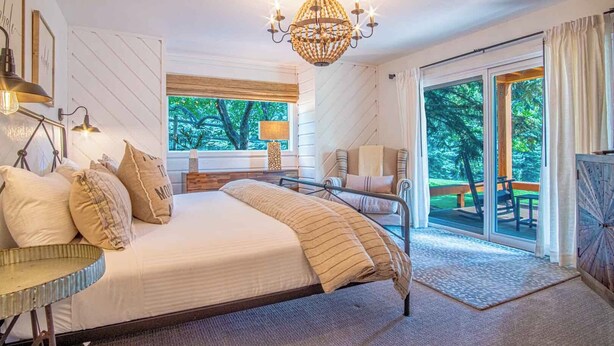 Een slaapkamer met een groot bed, een kroonluchter, uitzicht op het omliggende landschap en een raam met jaloezieën.
