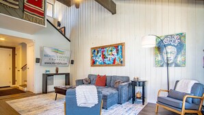 Un salon avec un canapé bleu, un fauteuil gris, un tableau abstrait aux couleurs vives et une enseigne indiquant « Michael's Vacation Rentals ».