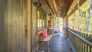 A wooden porch with benches and tables, a wooden railing, and a view of trees. - Board's Sunset Ranch - Sawtooth National Forest (Ketchum)