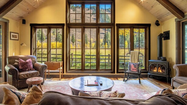 A cozy living room with a fireplace, large windows, and a high ceiling. - Board's Sunset Ranch - Sawtooth National Forest (Ketchum)