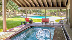 Une piscine extérieure couverte avec un jacuzzi, entourée de chaises rouges et d’une petite table.