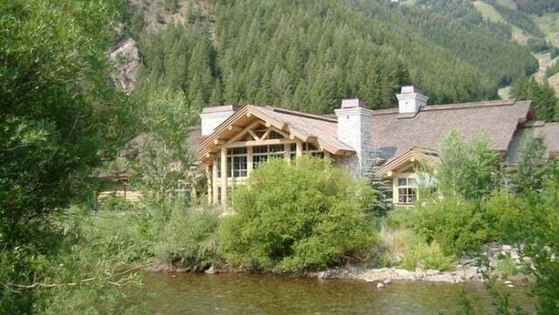 Un chalet au décor rustique, situé au bord d’une rivière, avec une forêt en arrière-plan.