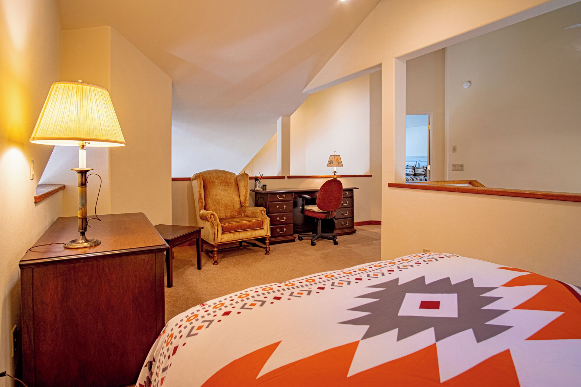 A hotel room with a bed, a desk, a chair, a lamp, and a large mirror.
