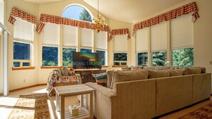 A sunlit living room with a large sofa, a small table, and a TV screen displaying 'Michael's Vacation Rentals'. - Sunflower Lane - 4BD Sun Valley Retreat + Resort Amenities (Sun Valley)