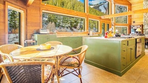 A spacious kitchen with large windows, a dining area with wicker chairs, and a stone accent wall. - River House - 4BD Riverfront, Hot Tub, Near SV Ski Lifts! (Ketchum)