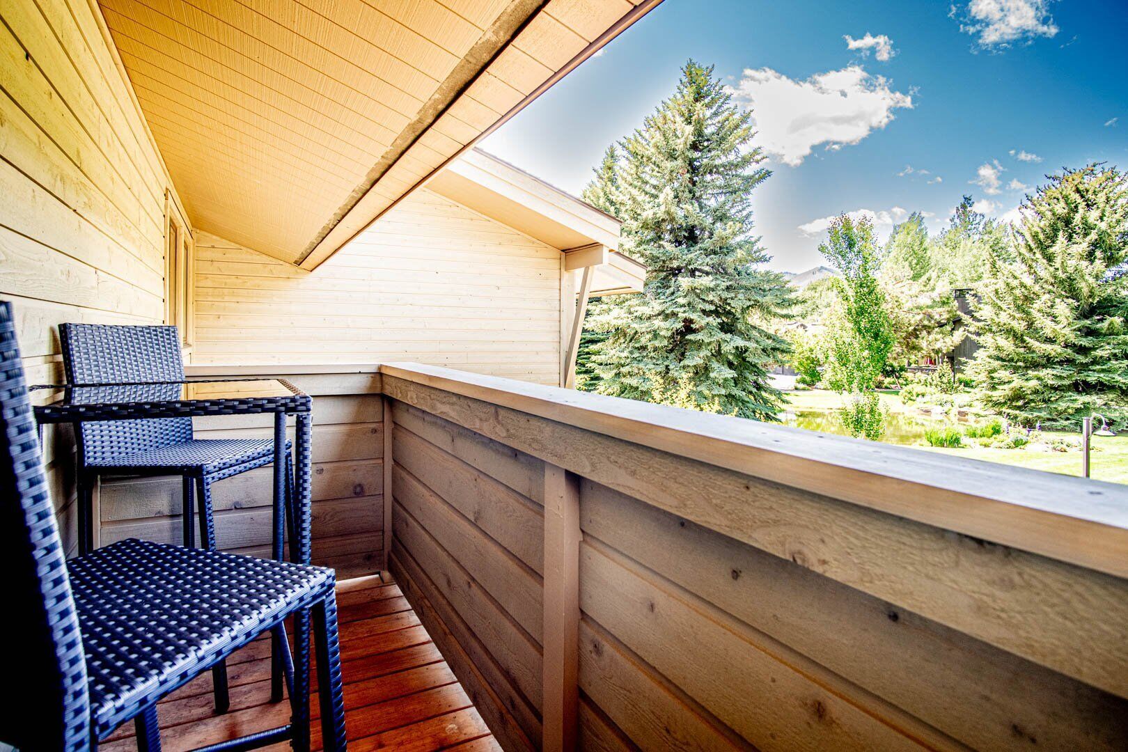 A wooden balcony with a view of a forest and a clear sky.