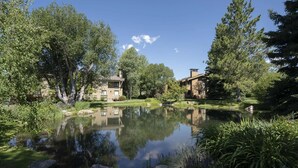 A tranquil pond surrounded by lush greenery and two stone buildings with chimneys, reflecting the clear blue sky. - Creekside 1273 - Nr Ski + Sun Valley Rec Passes (Sun Valley)