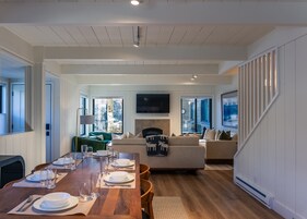 Amplia sala de estar con una mesa de comedor de madera dispuesta para cuatro personas, un sofá y un televisor montado en la pared.