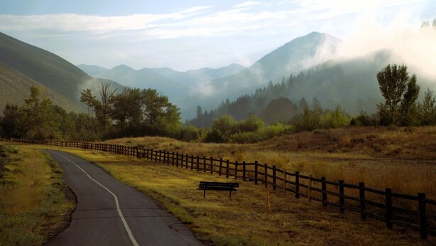 A winding road with a wooden fence and a bench, surrounded by mountains and fog. - Creekside 1294 - Nr Ski + Sun Valley Rec Passes (Sun Valley)