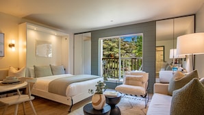 A modern bedroom with a large bed, a sitting area with a sofa and chairs, a small table, and a balcony with a view of trees. - Angani Studio - Elkhorn Resort Amenities Included (Sun Valley)
