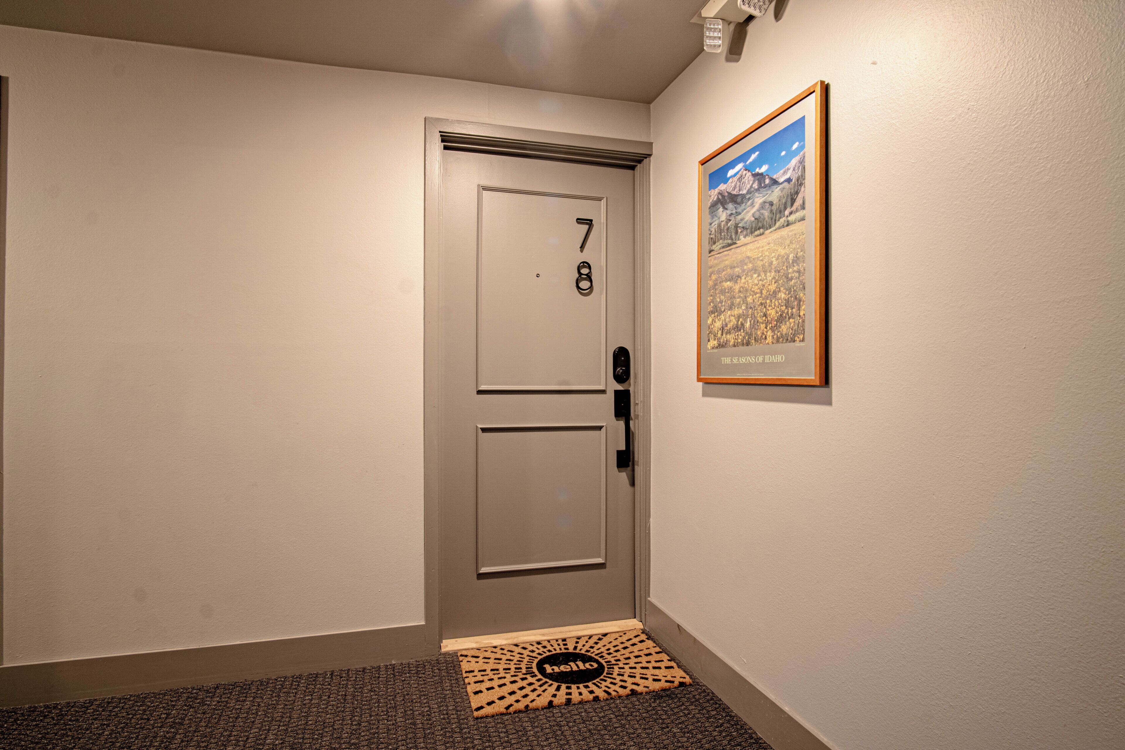 A hallway with a door marked with the number 78, a doormat with the word "hello", and a framed picture on the wall.