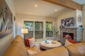 A living room with a stone fireplace, a television, and a large window. - Stonehenge Condo - Nr Ski Lifts & Downtown! (Ketchum)