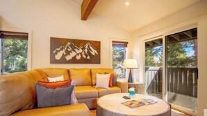 A living room with a sofa, a coffee table, a painting, and a view through a glass door. - Stonehenge Condo - Nr Ski Lifts & Downtown! (Ketchum)