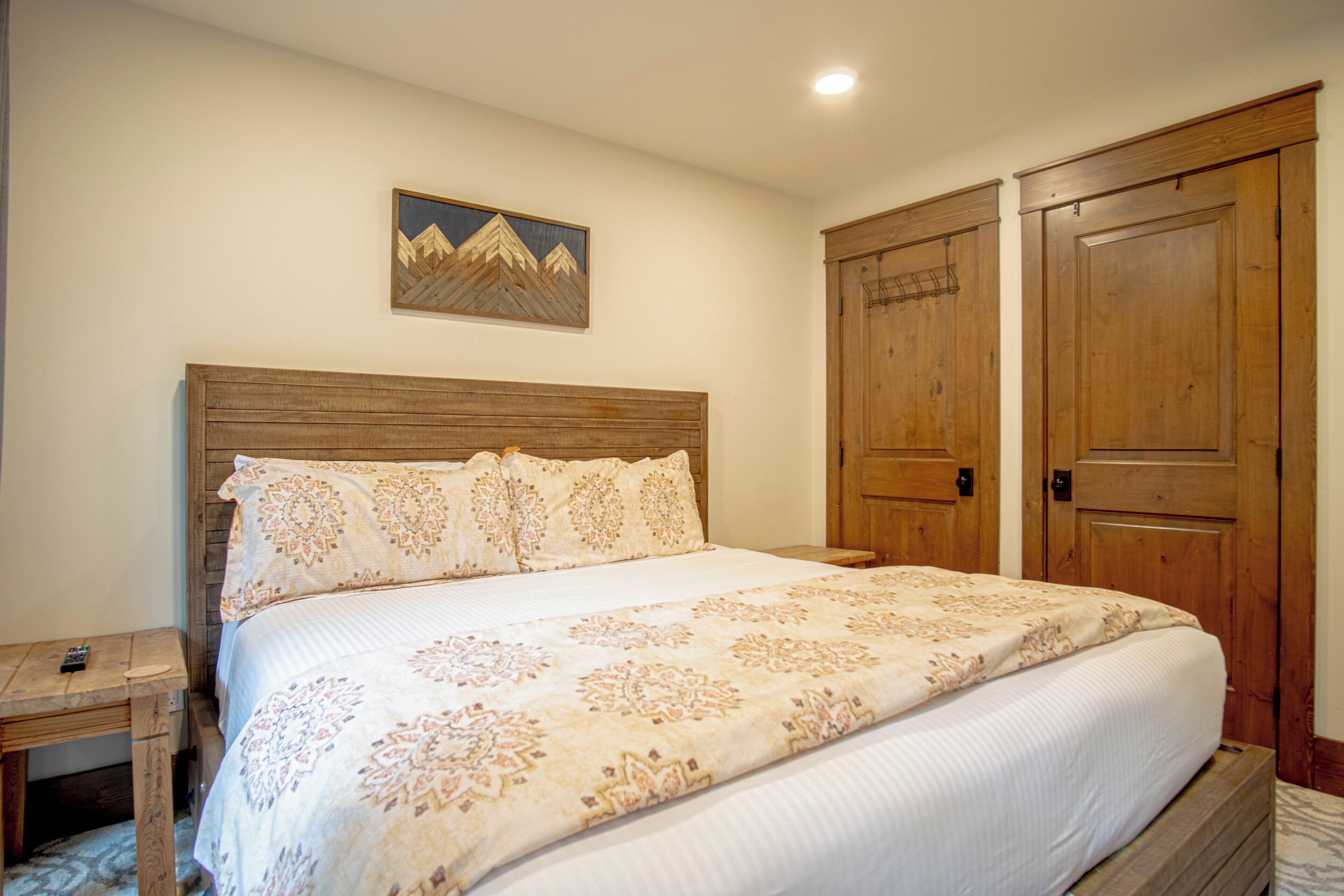 Une chambre à coucher avec une tête de lit en bois, un lit recouvert d’une literie à motifs, une table de chevet et une armoire en bois.