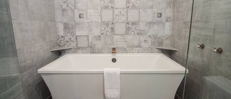 A bathroom with a freestanding bathtub, tiled walls, and a shower area.