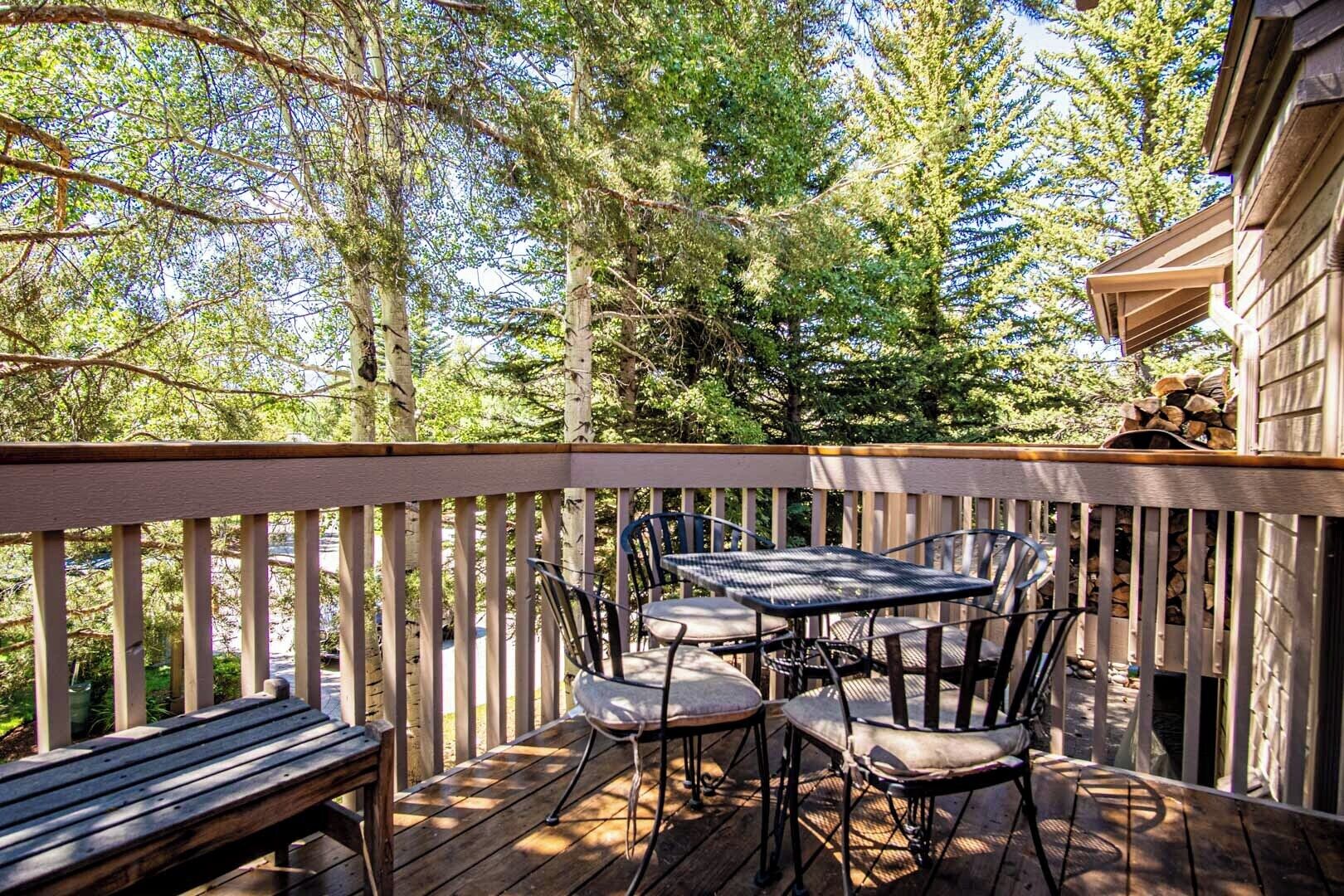 Une terrasse en bois avec une table et des chaises, entourée d’arbres.