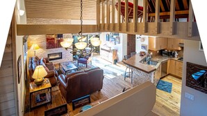 A spacious loft with a high ceiling, exposed wooden beams, a fireplace, a dining area, and a kitchen with wooden cabinets. - 2BD Fairway Nine Golf Condo + Free Resort Amenities (Sun Valley)