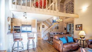 A spacious living area with a high ceiling, a leather sofa, a dining area with bar stools, and a kitchen with modern appliances. - 2BD Fairway Nine Golf Condo + Free Resort Amenities (Sun Valley)