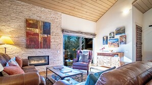 A cozy living room with a stone wall, leather furniture, a fireplace, and a view through large windows. - 2BD Fairway Nine Golf Condo + Free Resort Amenities (Sun Valley)