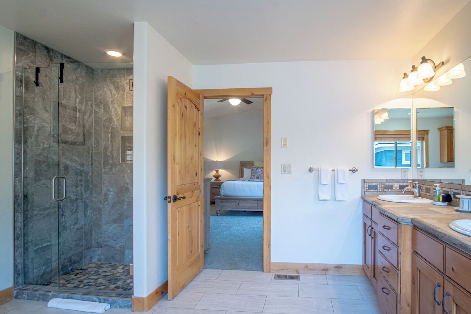 A modern bathroom with a glass shower enclosure, wooden door, and a large mirror.