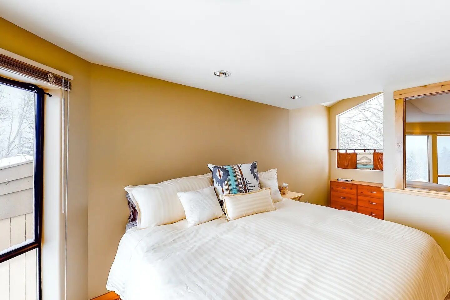 Quarto com uma cama grande, cômoda e janela com vista para árvores.