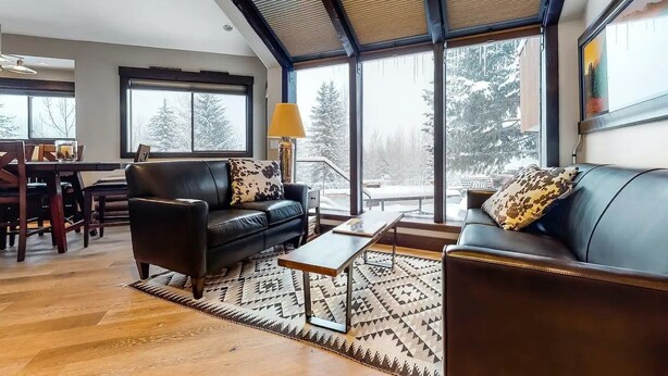 Ein modernes Wohnzimmer mit einer schwarzen Ledersofa, einem gemusterten Teppich und einem Essbereich mit Holztisch und Stühlen.