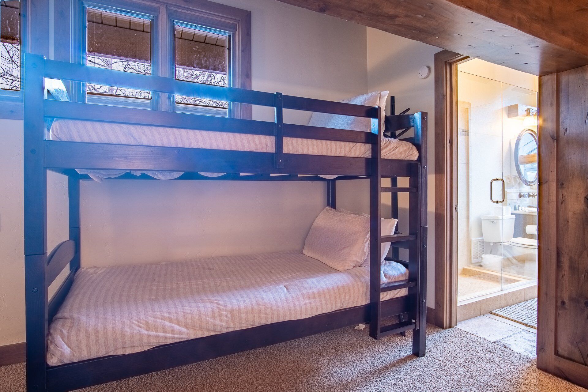 A bunk bed in a room with a wooden ceiling and a bathroom visible through an open door.