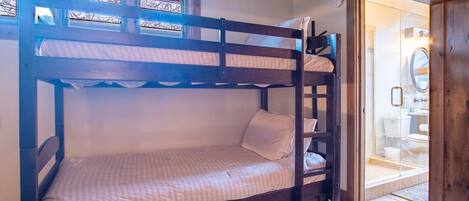 A bunk bed in a room with a wooden ceiling and a bathroom visible through an open door.