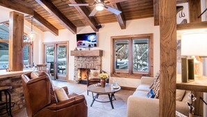 A cozy living room with a stone fireplace, leather sofas, a wooden ceiling, and large windows. - Sv154 - Walk to Lifts & Town - Hot Tub & Pool (Ketchum)
