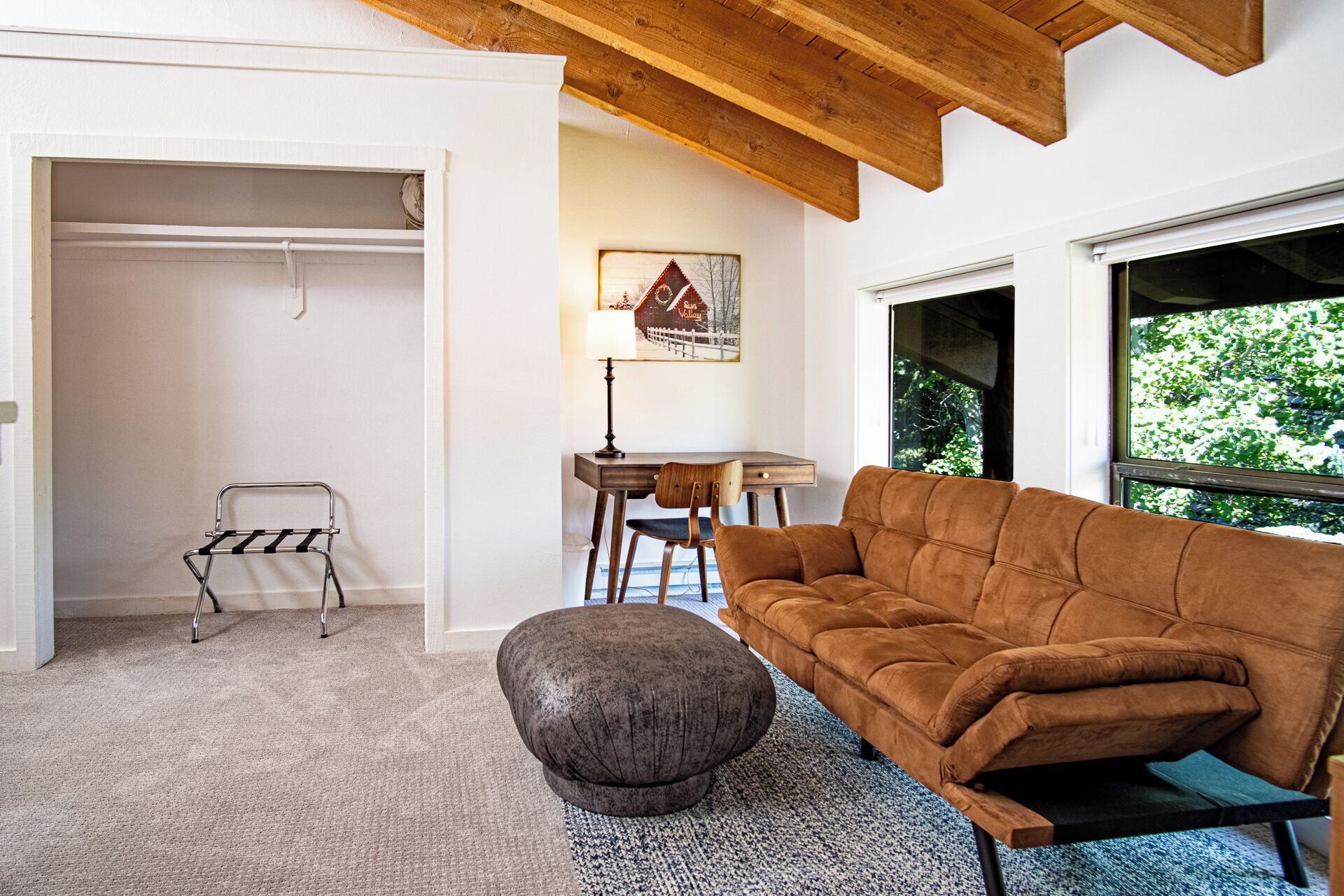 Una sala de estar moderna con un sofá marrón, un reposapiés gris, una mesa de centro de madera y una zona de comedor con una silla y una mesa de madera.