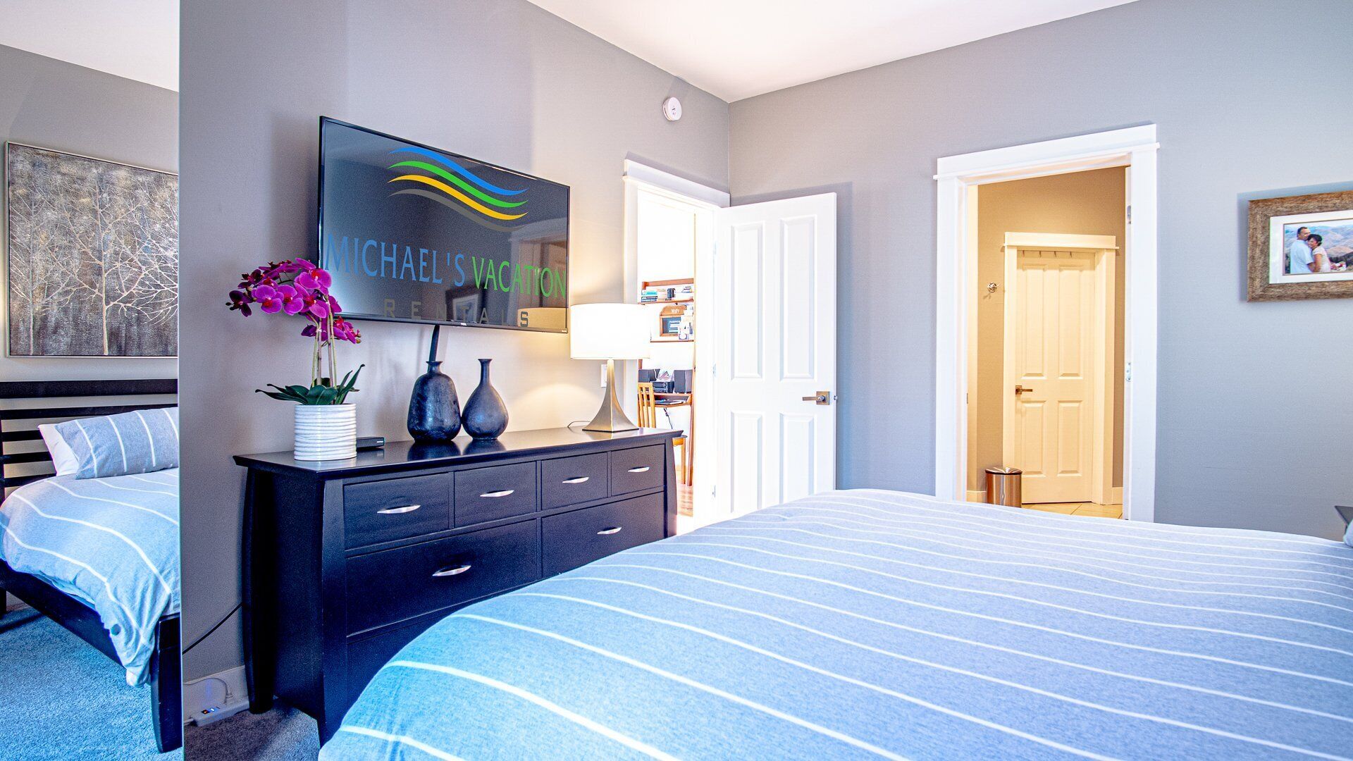 A bedroom with a bed, a dresser, a TV, and a door leading to another room.