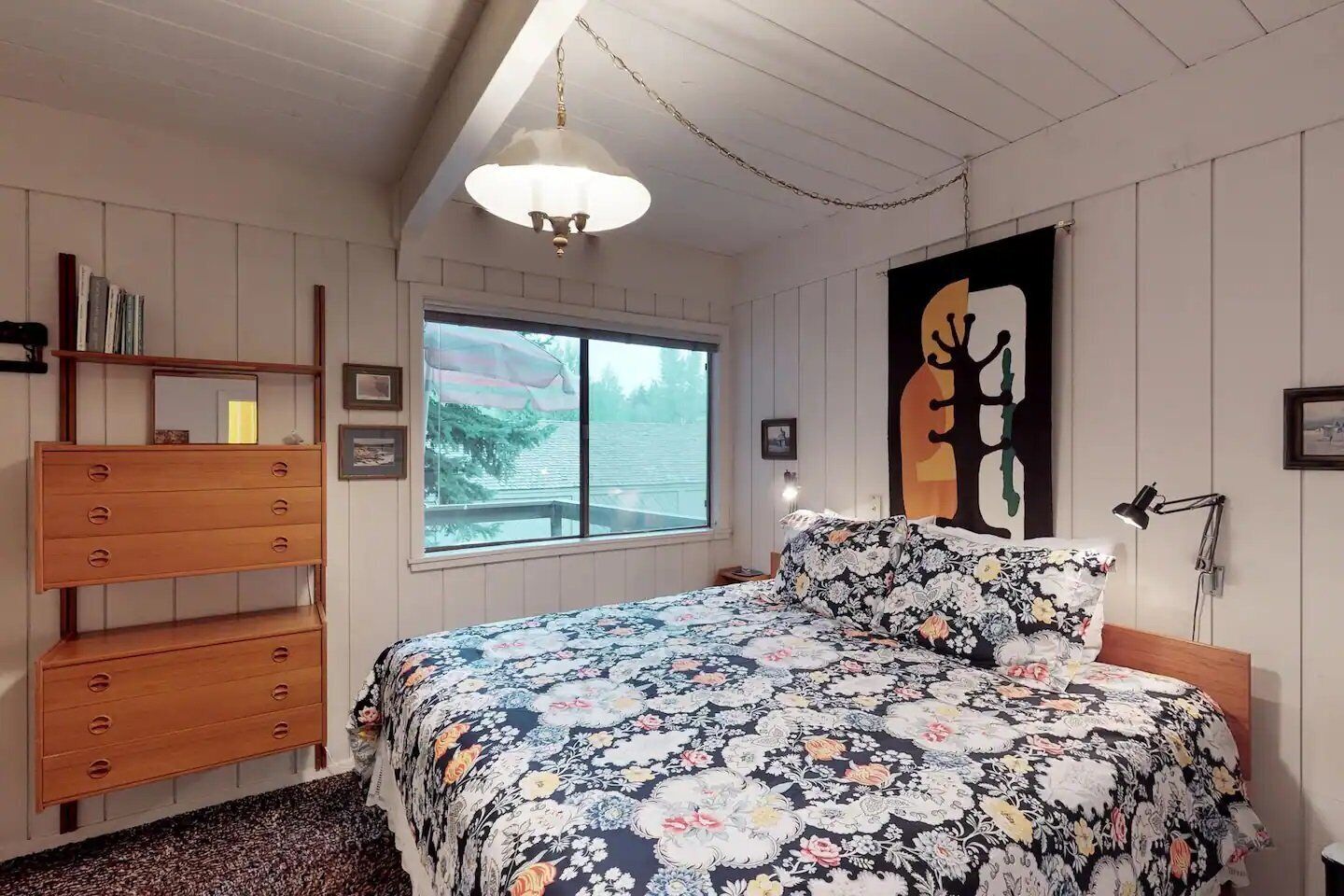 A bedroom with a bed, wooden dresser, and a large window.