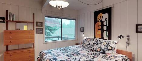 A bedroom with a bed, wooden dresser, and a large window.