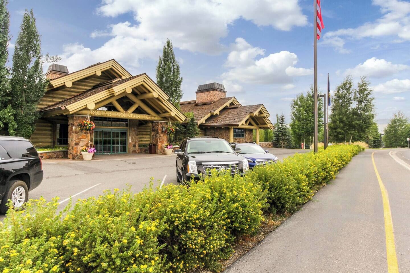 Ein Chalet mit steinverkleideter Fassade, einem überdachten Eingangsbereich und einem Parkplatz mit mehreren Autos.