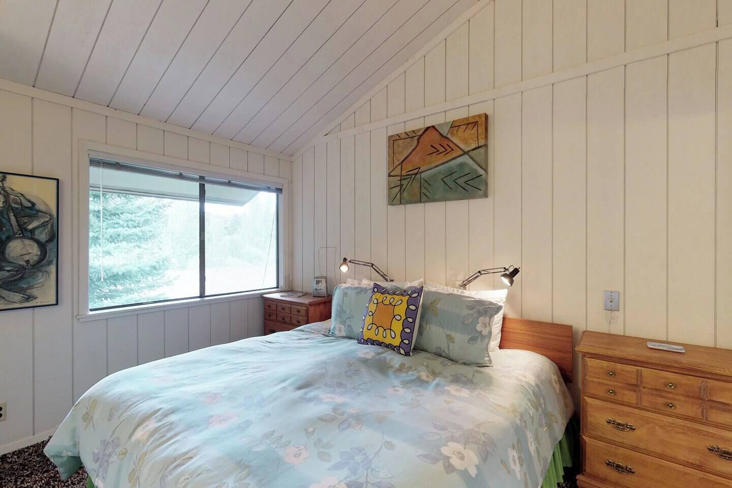 Une chambre à coucher avec un lit, une table de chevet, une commode, une fenêtre et un tableau accroché au mur.