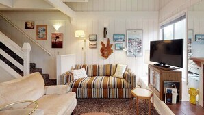 Een woonkamer met een gestreepte bank, een televisie en lijstjes met foto's aan de muur.