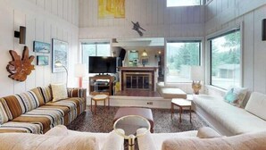Een ruime woonkamer met een open haard, grote ramen en een hoge plafond.