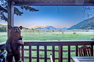 Una terraza de madera con vistas a un campo cubierto de hierba y montañas al fondo.