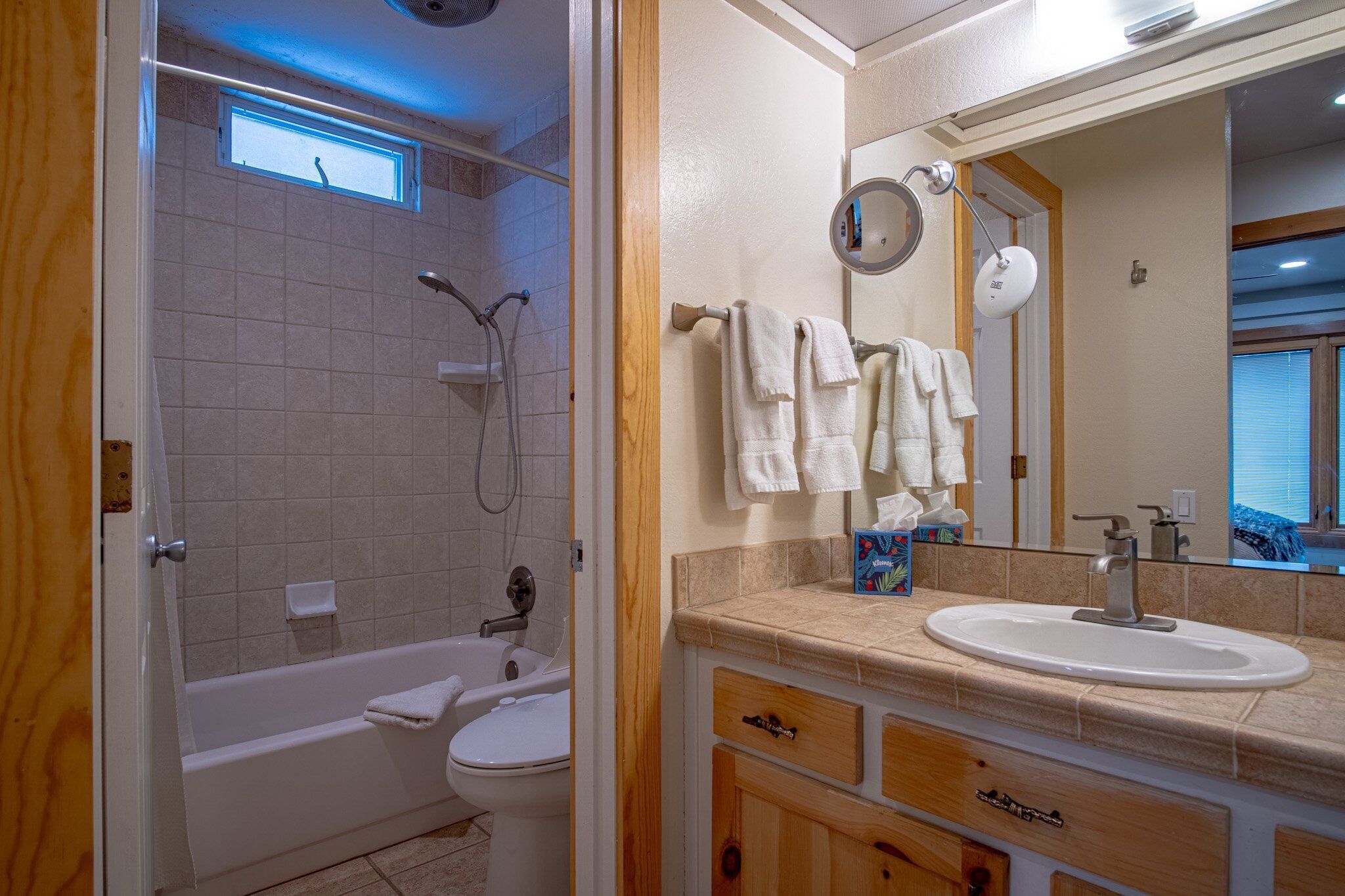 A bathroom with a bathtub, toilet, and sink. There is a window above the bathtub and a mirror above the sink.