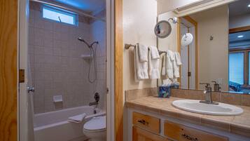 A bathroom with a bathtub, toilet, and sink. There is a window above the bathtub and a mirror above the sink.