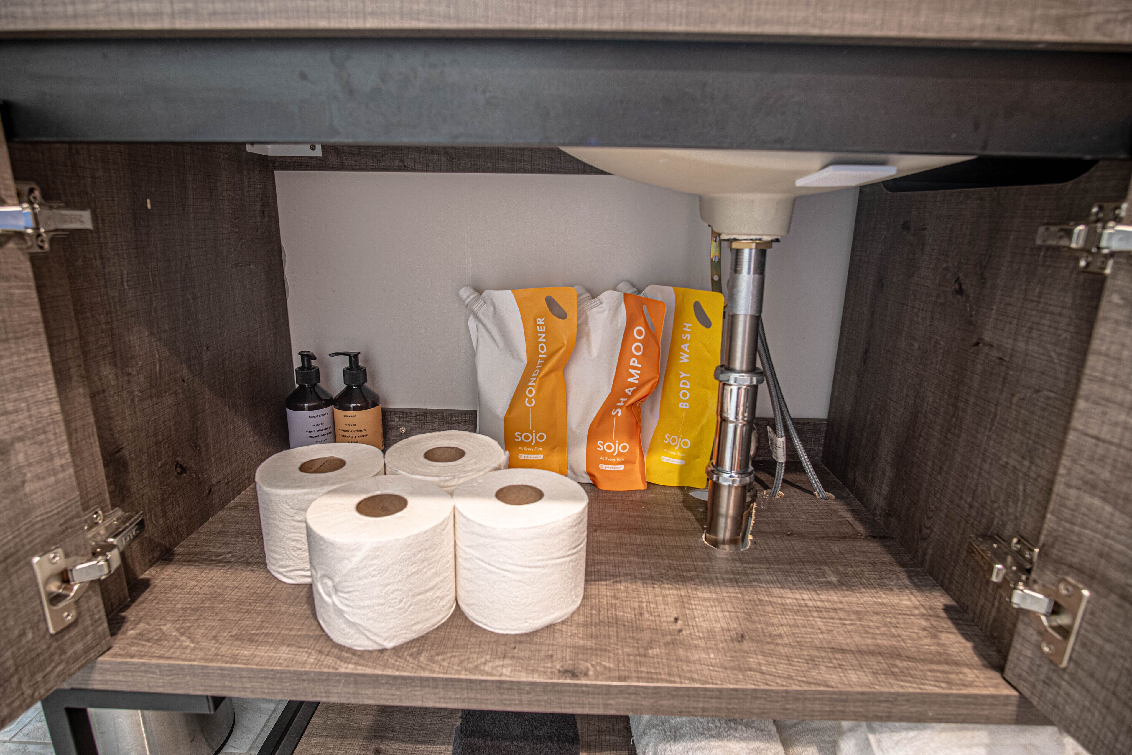 Een badkamer met een houten wastafel, meerdere toiletrollen en diverse flessen shampoo en conditioner.