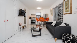 Uma sala de estar moderna com uma mesa de centro de vidro, um sofá preto e cadeiras laranja.