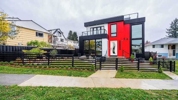 Uma casa moderna de dois andares com fachada vermelha e branca, cerca preta e um jardim bem cuidado.