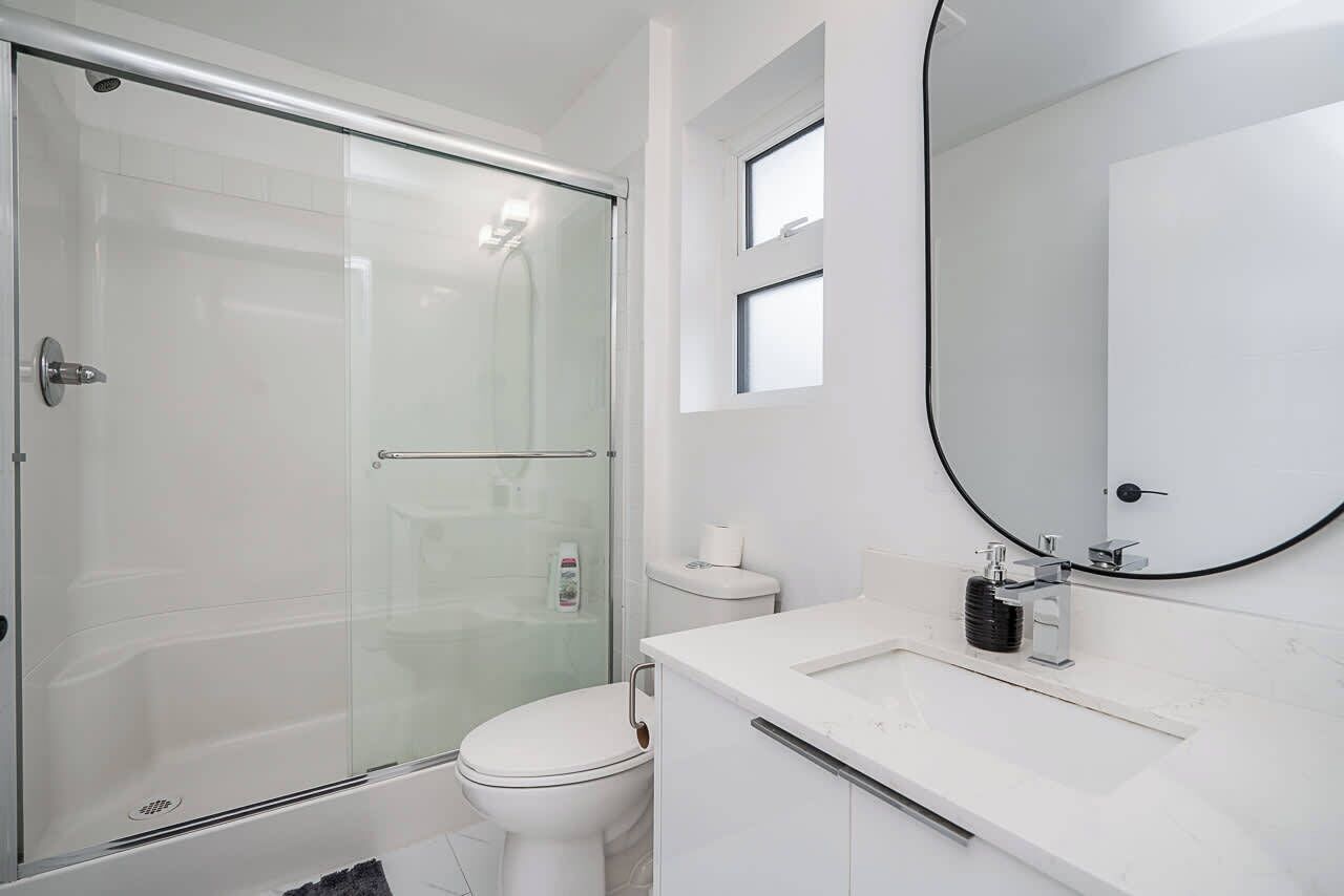 A modern bathroom with a glass-enclosed shower, a toilet, a sink with a mirror, and a window above the sink.