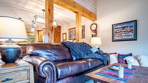Una sala de estar acogedora con un sofá de cuero, vigas de madera, una mesa de comedor con un mantel individual y un reloj en la pared.