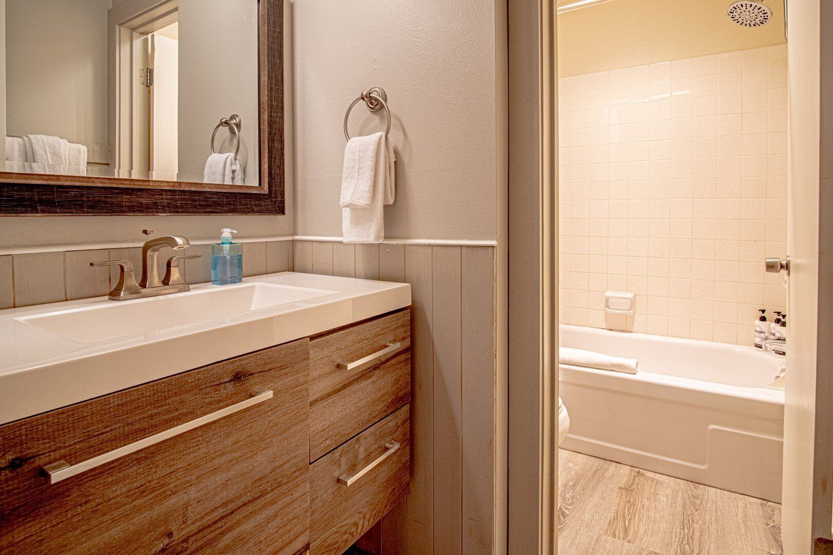 A bathroom with a wooden vanity, a mirror, a towel rack, and a bathtub.