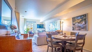 A spacious living room with a dining area, a piano, and a large painting. - 2BD Sweetwater Condo - Community Park, Pool + Hot Tub (Hailey)